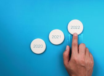 Jahreszahlen 2020 bis 2023 in drei Buttons aufsteigend angeordnet vor blauem Hintergrund. Ein Zeigefinger einer Hand zeigt von unten auf den Button 2022.